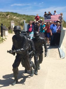 A group of people standing on the beaches of Normandy holding an American flag