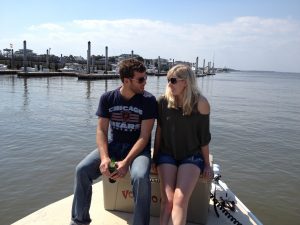 A man and a woman sitting on a dock over some water. They're facing each other and talking.