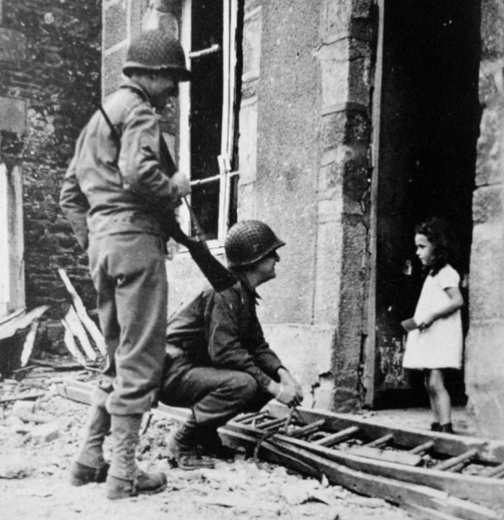 French girl in a doorway surrounded by rubble talking to two soldiers